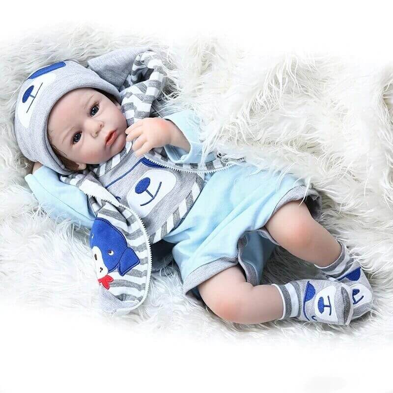 Le bébé reborn garçon Adam porte un bel ensemble bleu et gris.